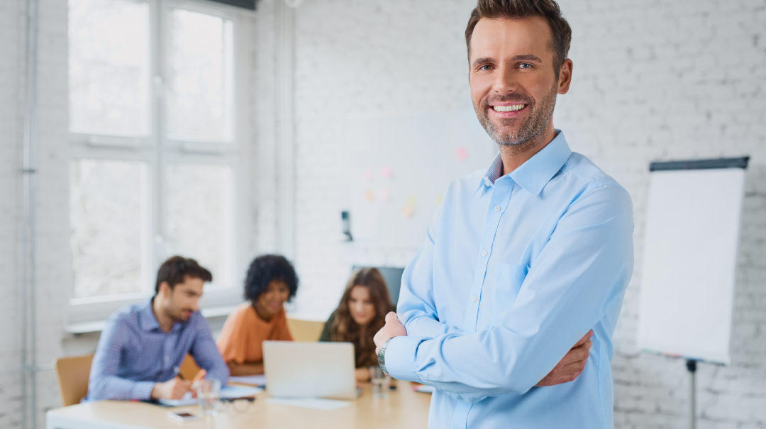 Happy businessman standing in the office with coworkers in the b