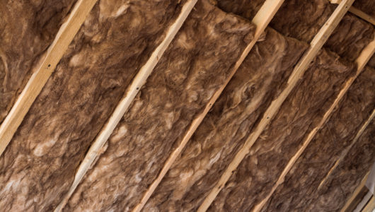 Brown glass wool in a wooden frame on a inclined wall near the wooden ceiling in a private house. Warming the house with fiberglass.