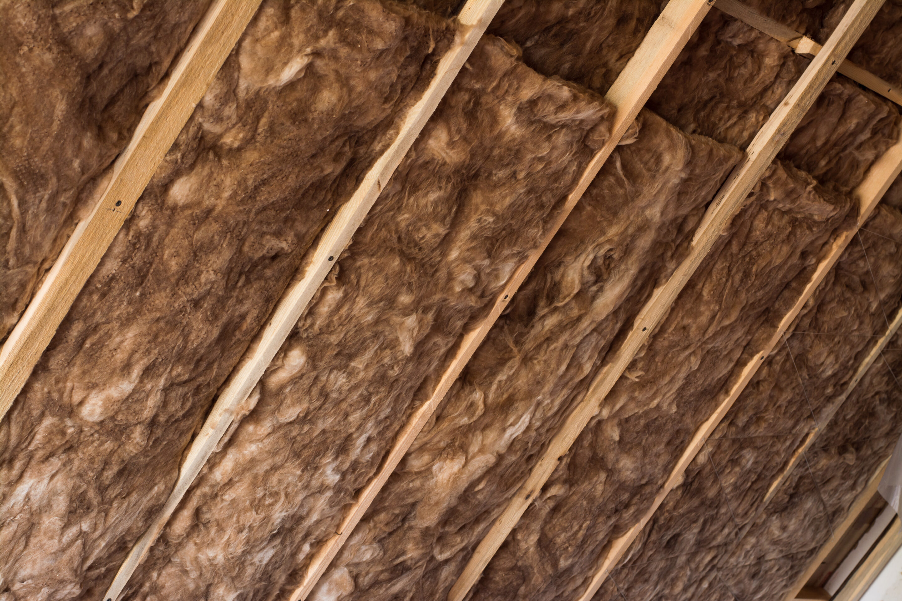Brown glass wool in a wooden frame on a inclined wall near the wooden ceiling in a private house. Warming the house with fiberglass.