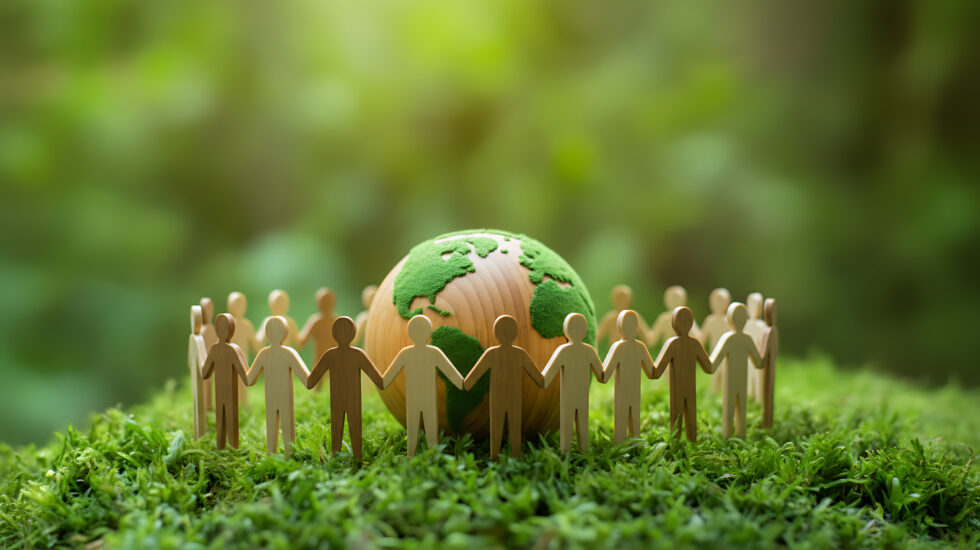 Wooden people figures holding hands around a globe on green moss